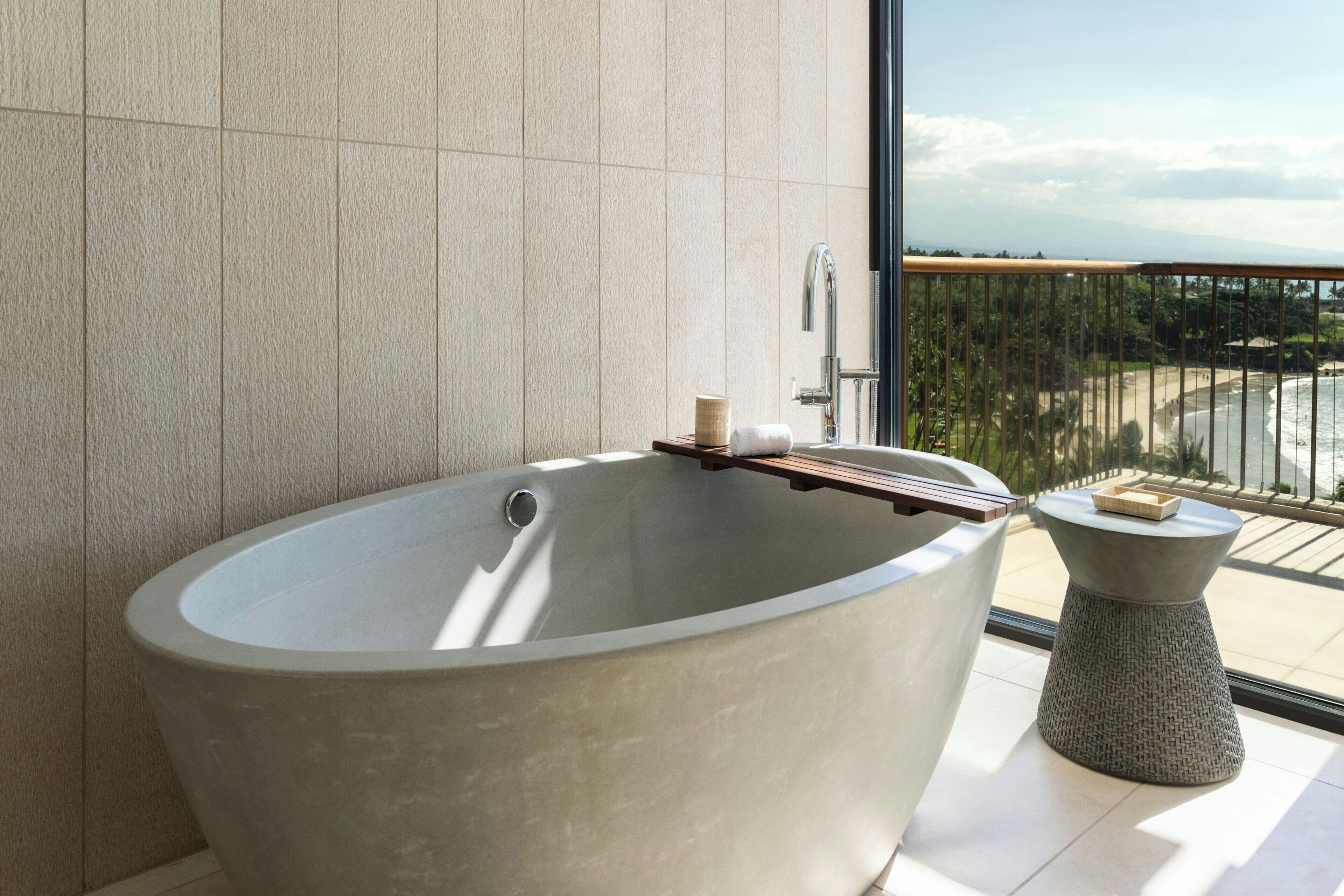 A modern bathroom with a freestanding bathtub, a wooden tray, and a small round table with toiletries.