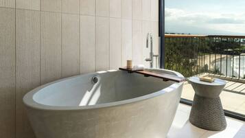 A modern bathroom with a freestanding bathtub, a wooden tray, and a small round table with toiletries.