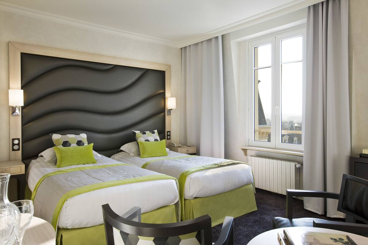Een hotelkamer met twee bedden, een groot raam, een bureau en een stoel.