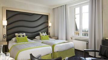 Une chambre d’hôtel avec deux lits, une grande fenêtre, un bureau et une chaise.