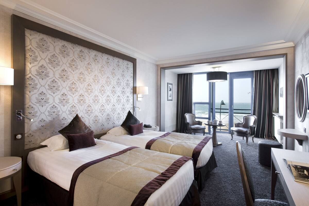 Een hotelkamer met twee bedden, een bureau, een stoel en uitzicht op zee.