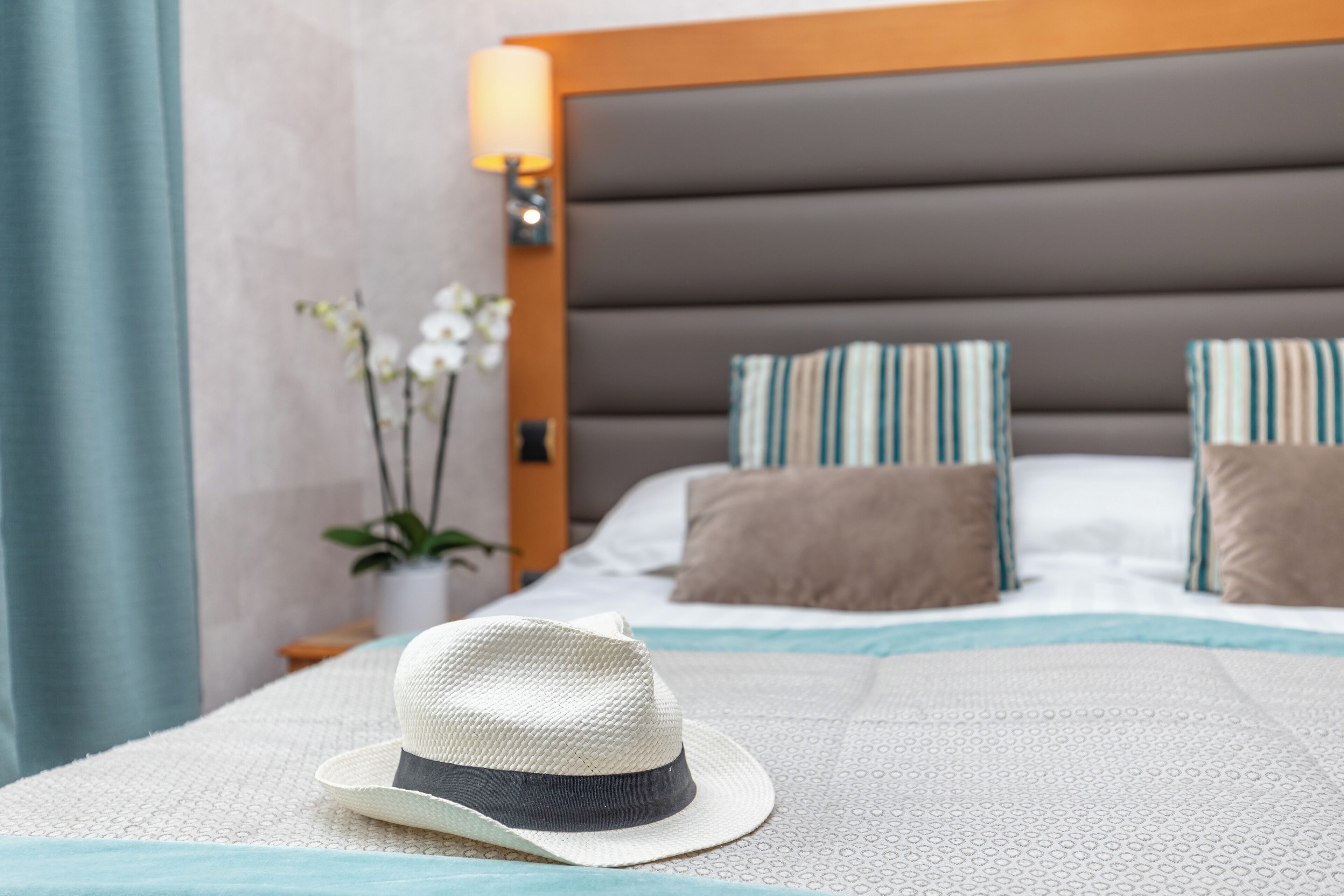 A neatly made bed with a white and blue patterned bedspread, a white hat on the bed, and striped pillows.