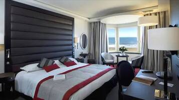 Una habitación de hotel con una cama grande, un escritorio, una silla, una lámpara y vista al océano.