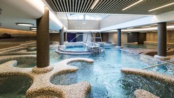 Une piscine intérieure aux murs recouverts de mosaïques, avec un escalier central et un panneau indiquant « AQUATONIC ».
