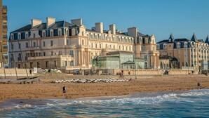 A beachfront hotel with multiple stories, a sandy beach in front, and boats lined up on the shore. - Grand Hôtel des Thermes (Saint-Malo)