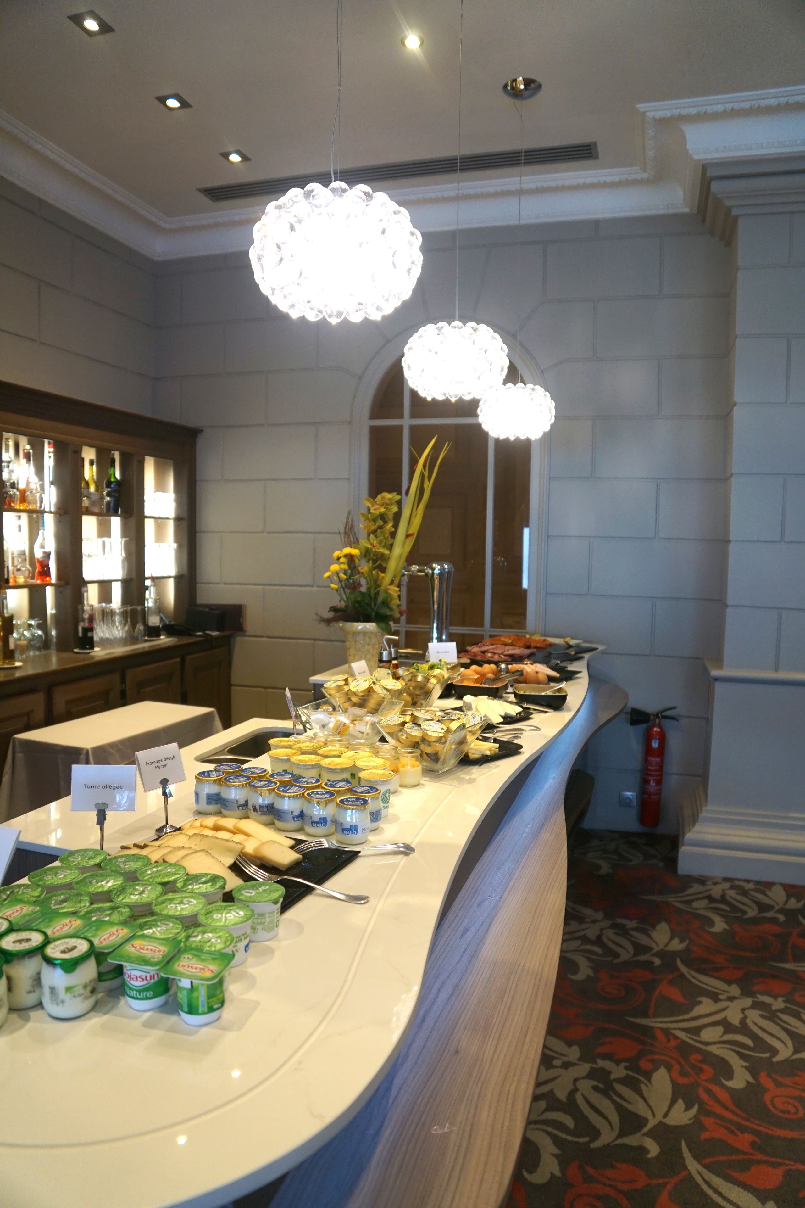 A buffet setup with various food items and condiments, a bar area with bottles, and a decorative vase with yellow flowers.