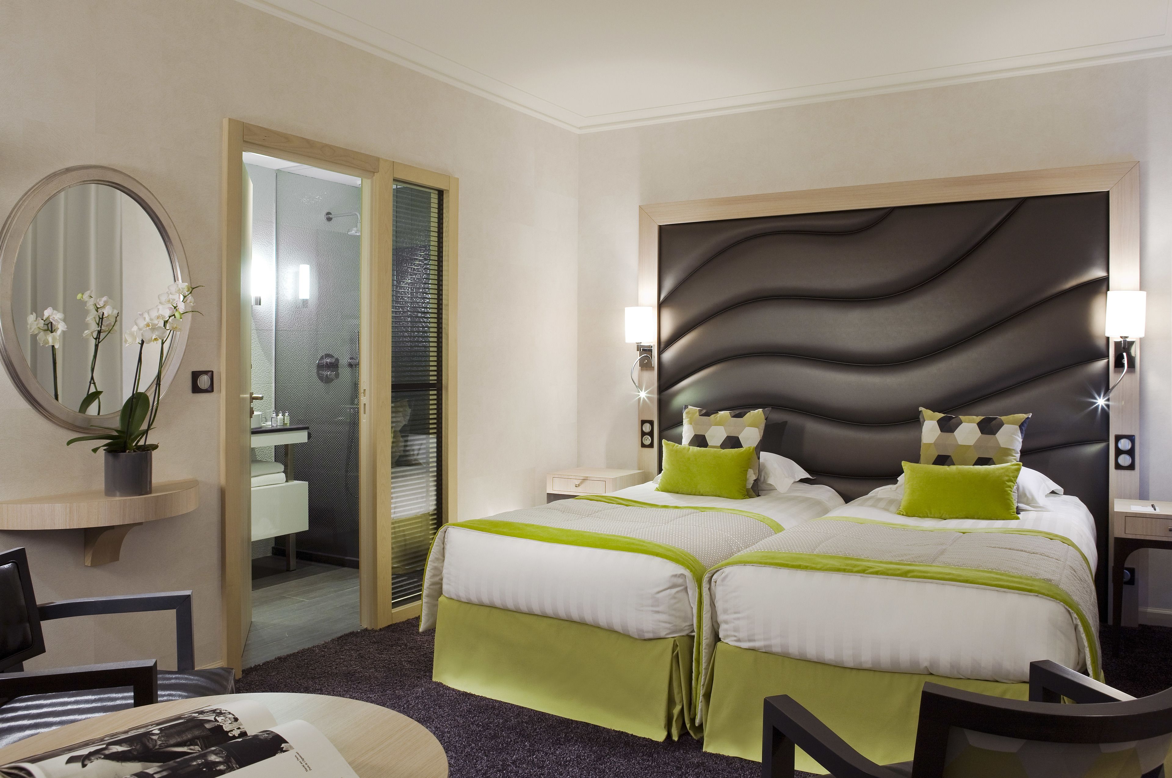 A hotel room with a double bed, a bedside table, a mirror, and a view of the bathroom.