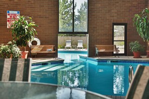 An indoor swimming pool with clear water, surrounded by brick walls, benches, and potted plants. - Coast Wenatchee Center Hotel (Wenatchee)