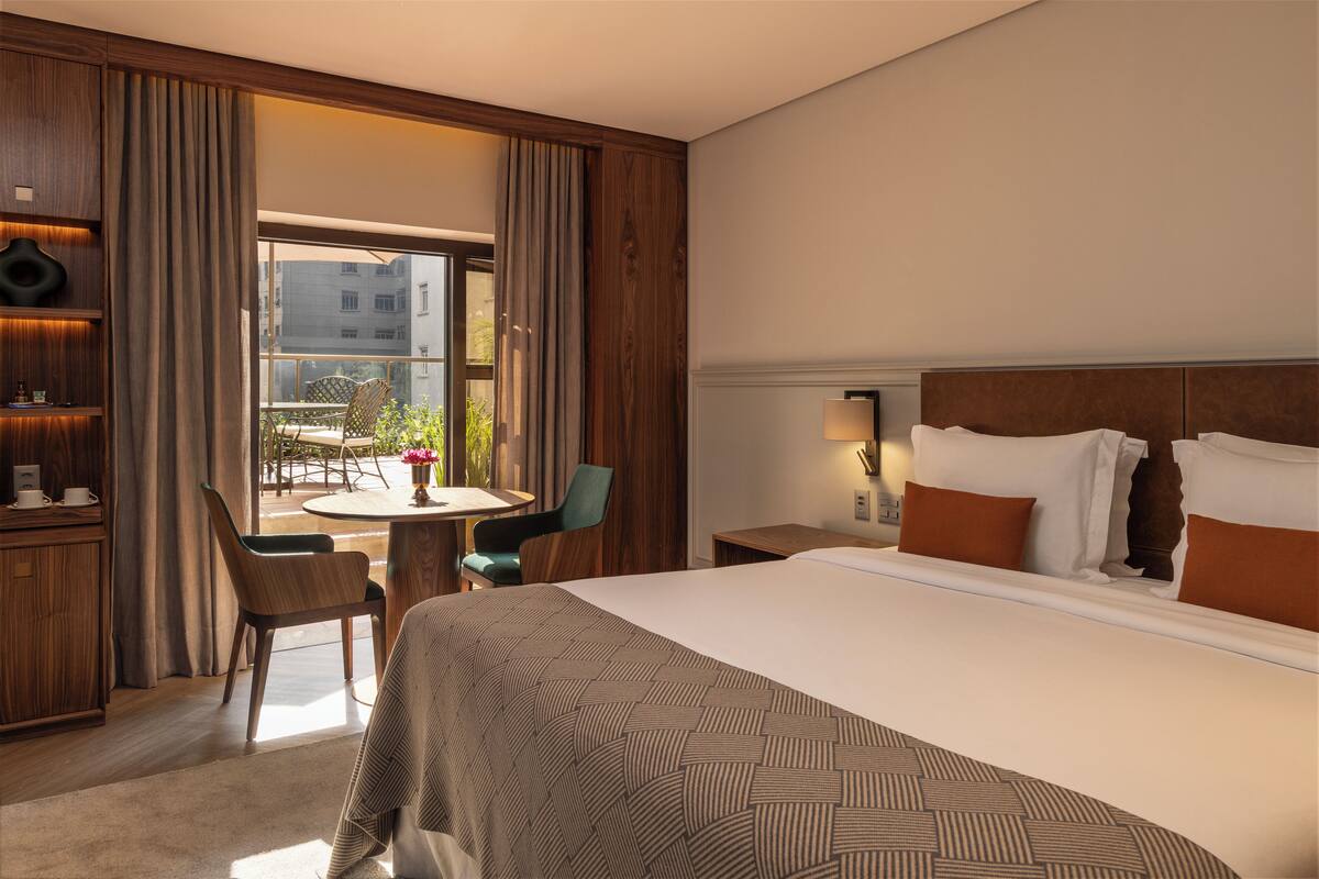 Een hotelkamer met een groot bed, een bureau met stoel, een kleine tafel met stoel en uitzicht op buiten.