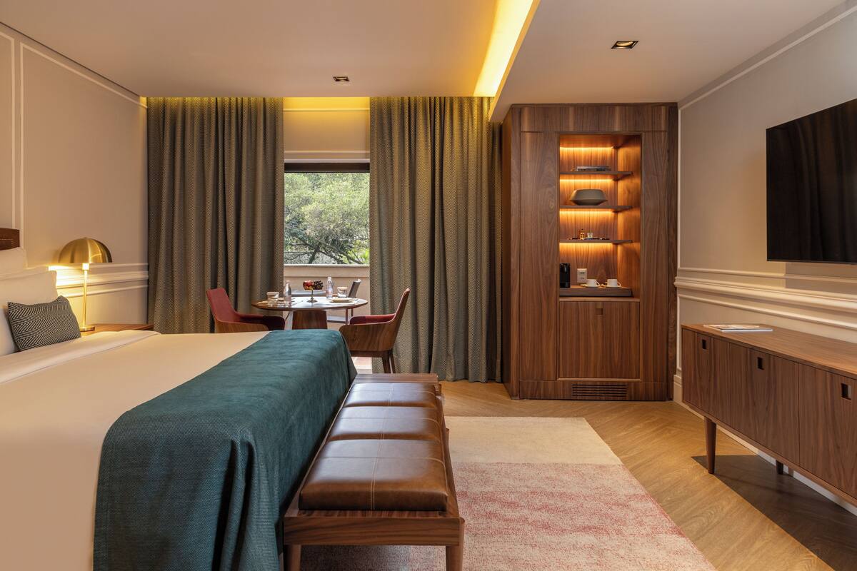 Een hotelkamer met een groot bed, een bankje, een bureau met stoel, een televisie en een houten kast.