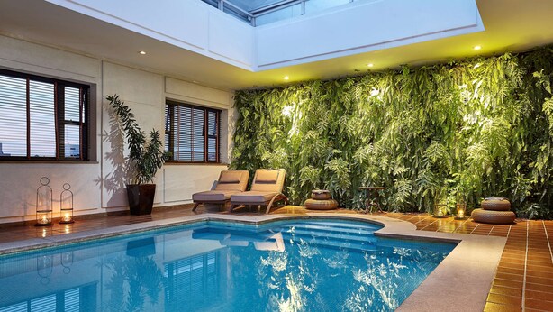 Piscina interna com vista para o teto, parede coberta de folhagem verde e cadeiras de descanso.