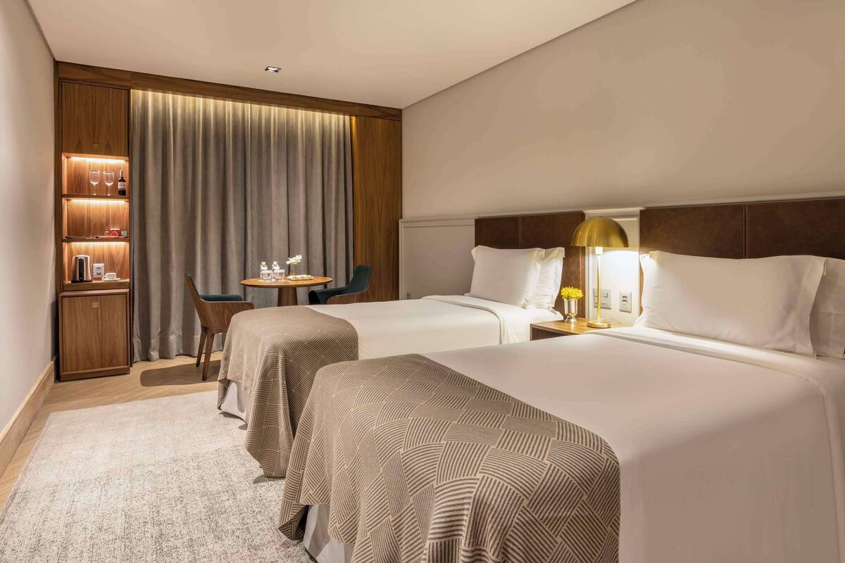 Een hotelkamer met twee bedden, een bureau, een stoel, een lamp en een minibar.