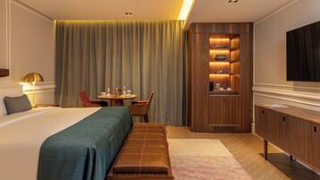 A hotel room with a large bed, a bench, a desk with a chair, a TV, and a wooden cabinet.