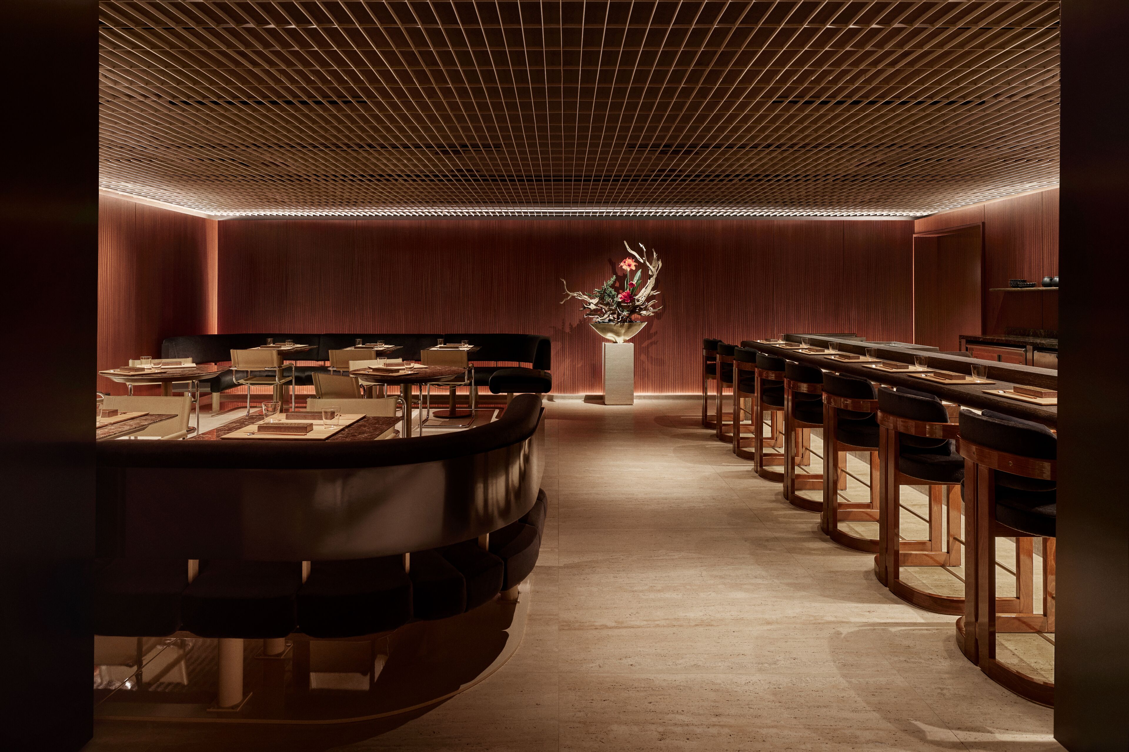 Un interior moderno con una larga recepción, sillas de madera y un centro de mesa con planta decorativa.