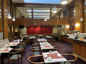 A hotel dining area with multiple tables and chairs, a buffet counter, and a high ceiling with skylights. - The Prince Kitano New York (New York)