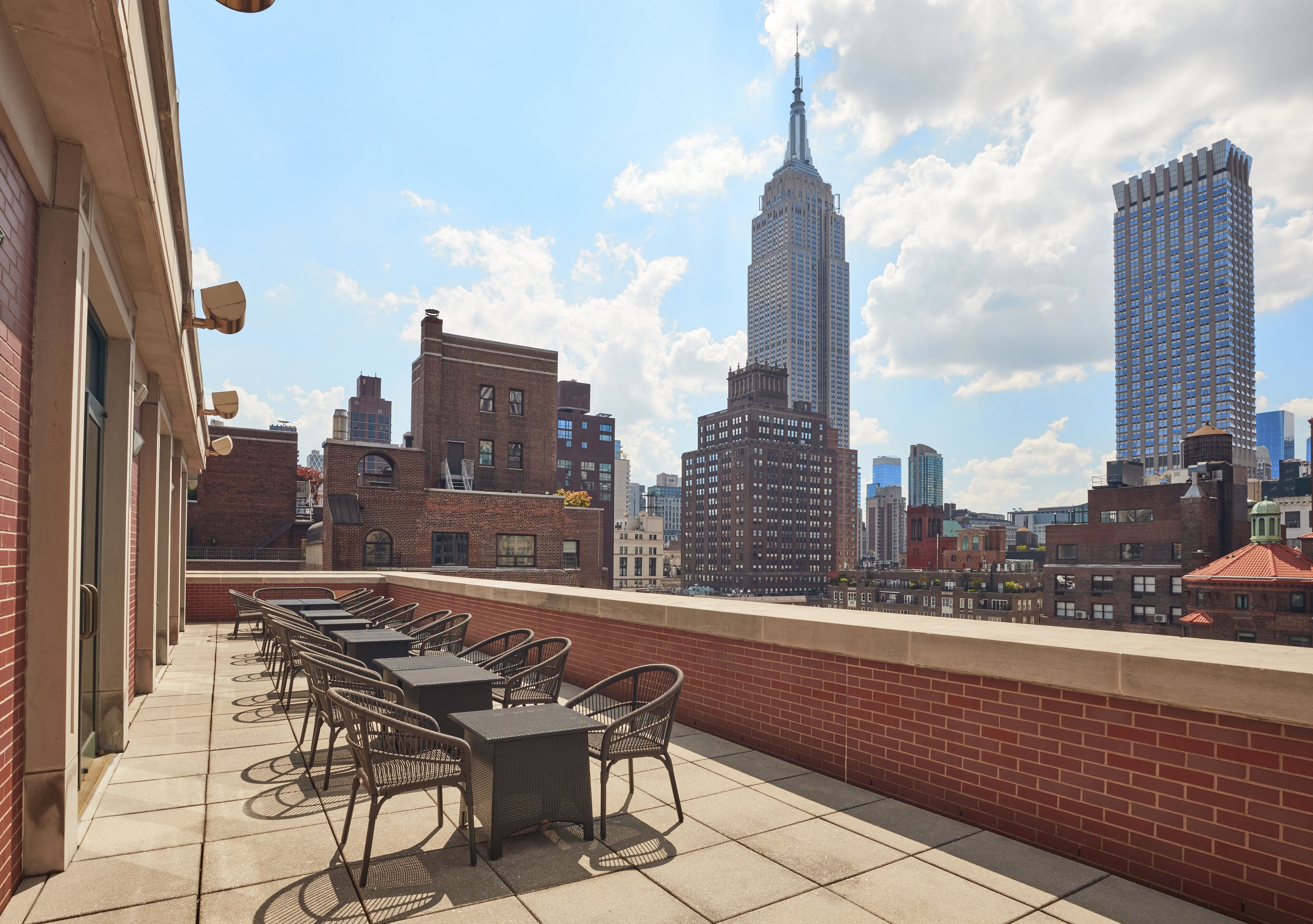 A rooftop terrace with outdoor seating, overlooking a cityscape with prominent buildings.