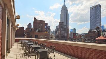 A rooftop terrace with outdoor seating, overlooking a cityscape with prominent buildings.