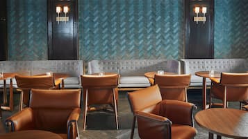 Un interior de restaurante con sillas de cuero, mesas redondas, un sofá gris y paredes con diseños.