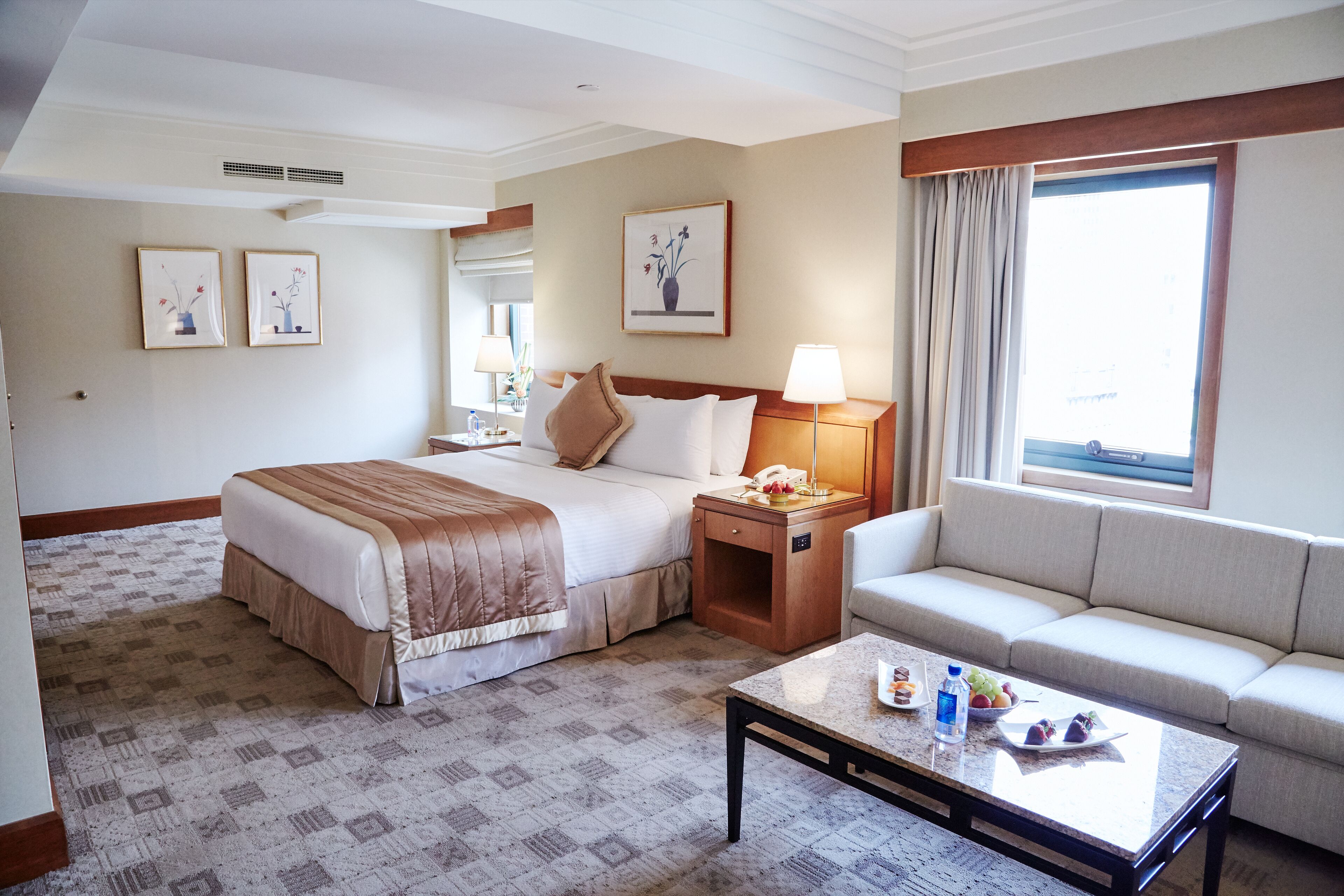 A hotel room with a bed, a sofa, a coffee table, and a window with curtains.