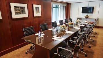 A conference room with a long table, chairs, framed pictures, a TV, and a window with curtains.