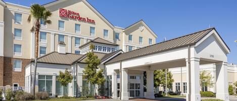 A Hilton Garden Inn with a covered entrance, a brick facade, and a clear blue sky.