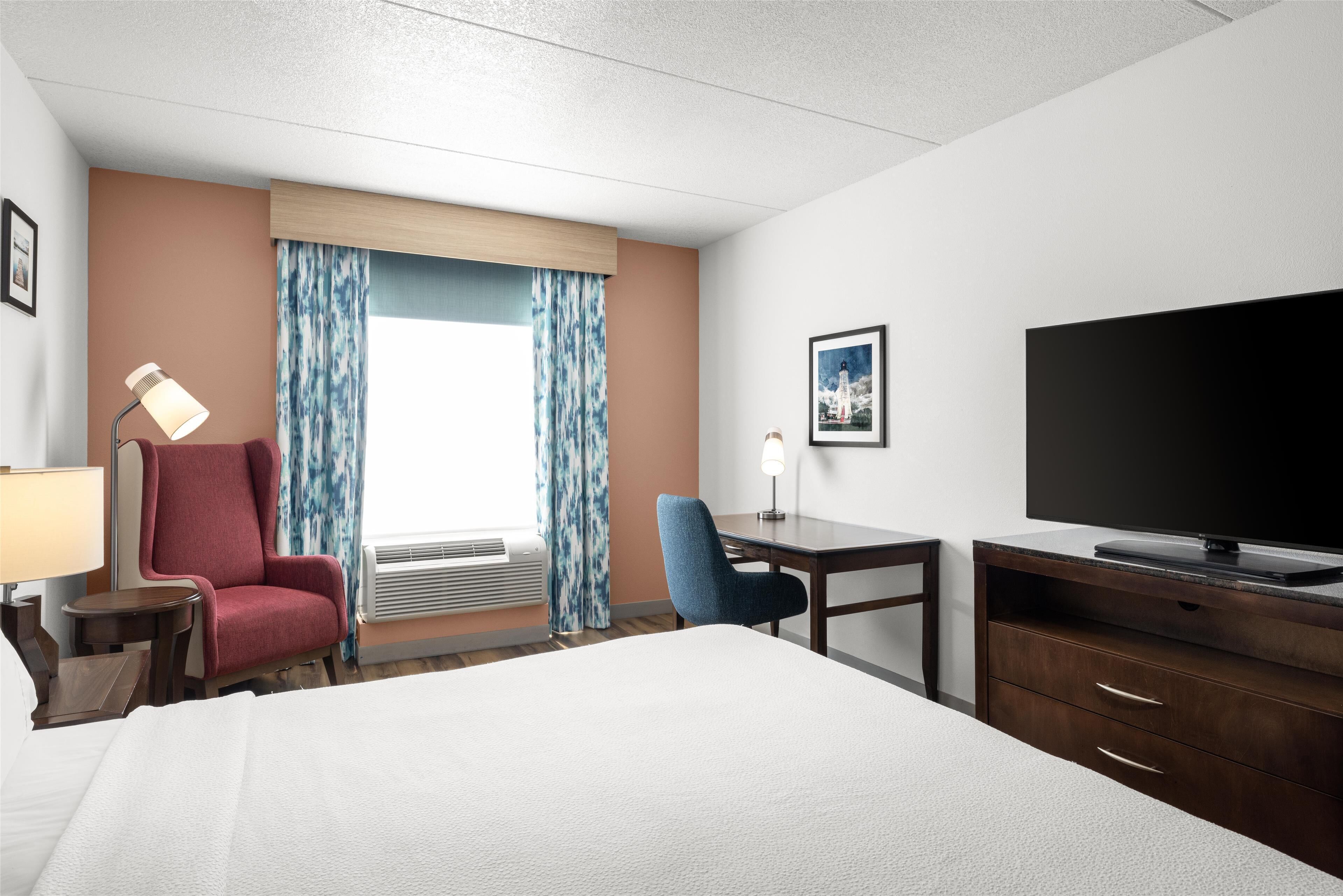 Une chambre d’hôtel avec un lit, un bureau, une télévision, une chaise et une fenêtre avec des rideaux.