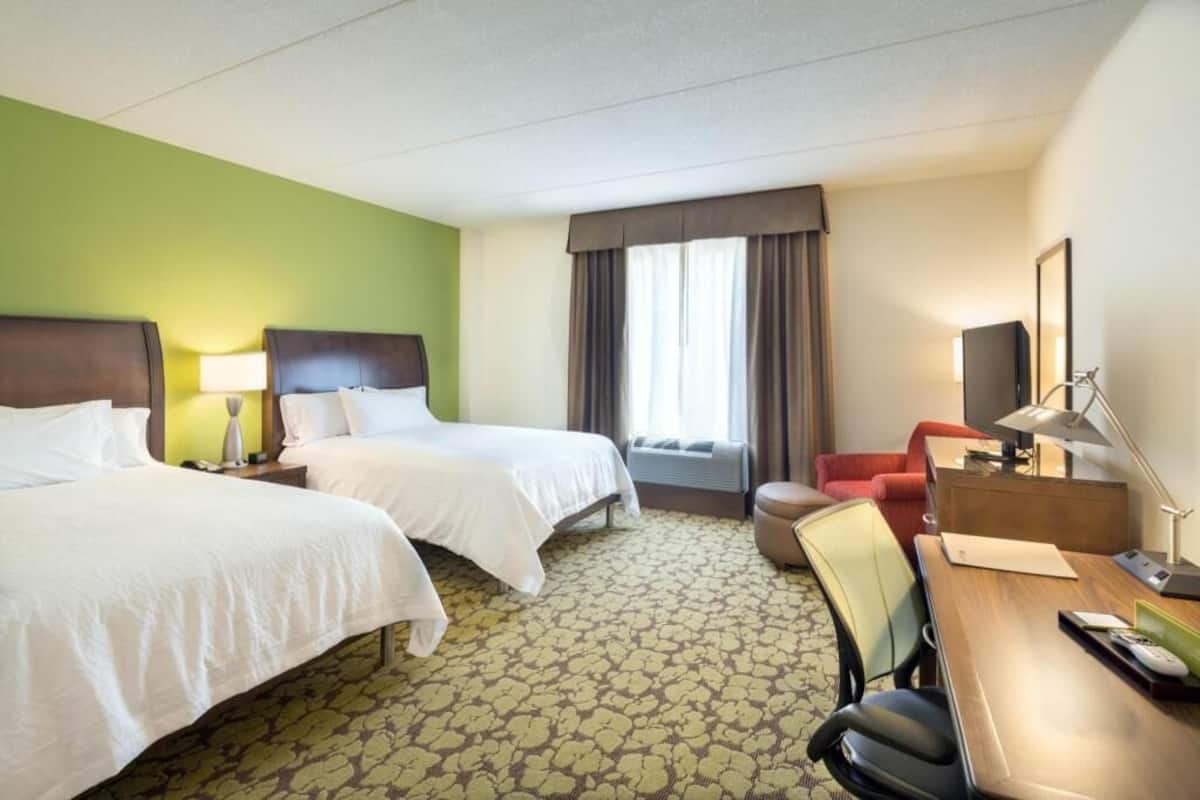 A hotel room with two beds, a desk, a chair, a television, and a window with curtains.