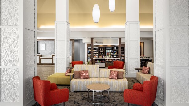 A lobby with a seating area featuring red chairs and a striped sofa, a FreeShop, and a bookshelf. - Hilton Garden Inn Pascagoula (Pascagoula)