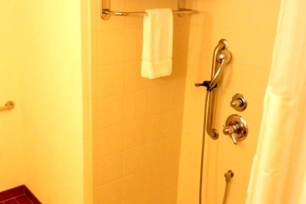 A small, tiled shower area with a glass shower door, a towel rack with towels, and a shower control panel.