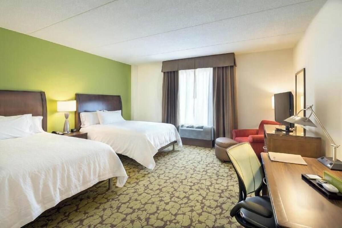 A hotel room with two beds, a desk, a chair, a TV, and a window with curtains.
