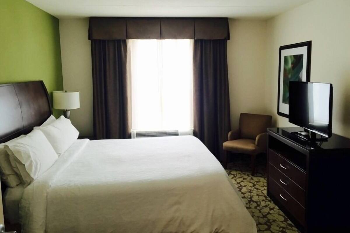 A hotel room with a large bed, a television, a chair, and a dresser.