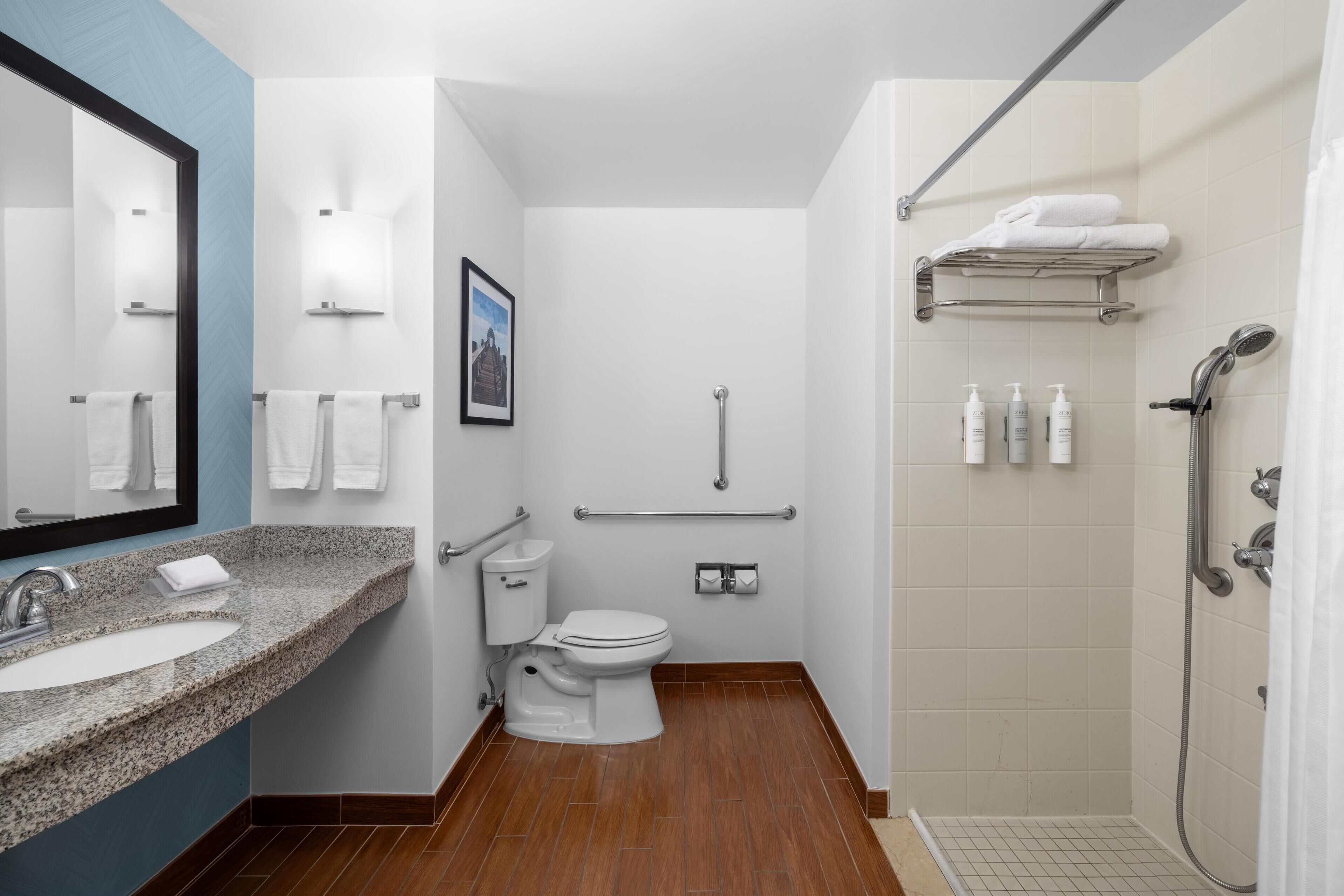 Un baño moderno con lavabo de granito, inodoro blanco y ducha a ras de suelo.