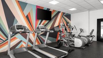 A gym with treadmills, elliptical machines, and a TV on the wall.