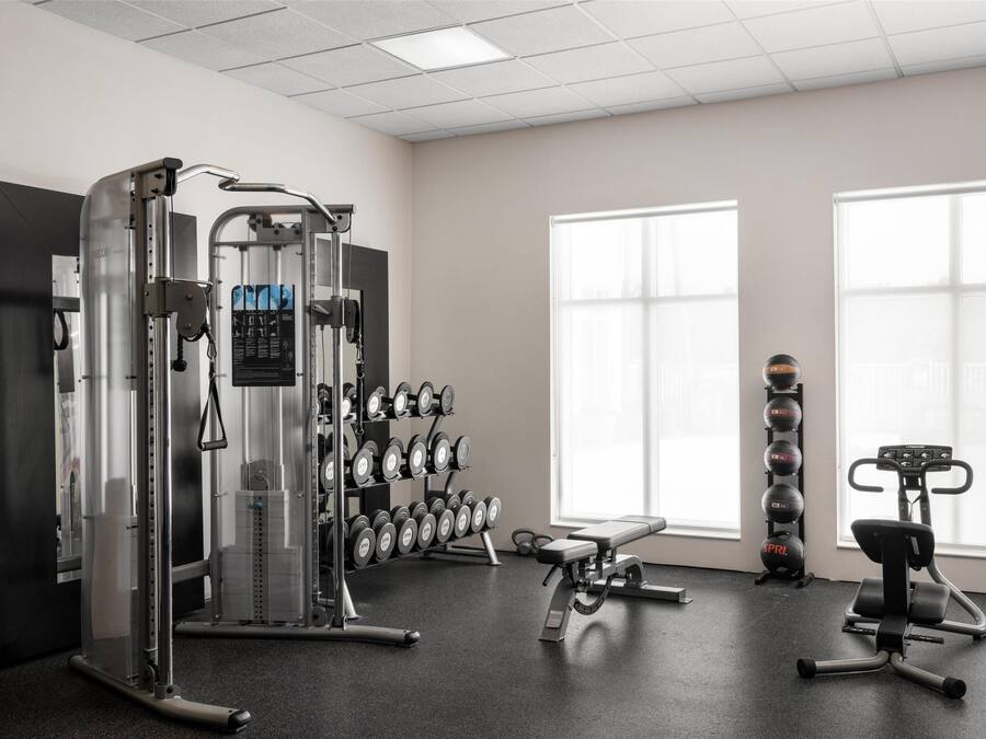 Un gimnasio con máquinas de pesas, mancuernas y una banca.