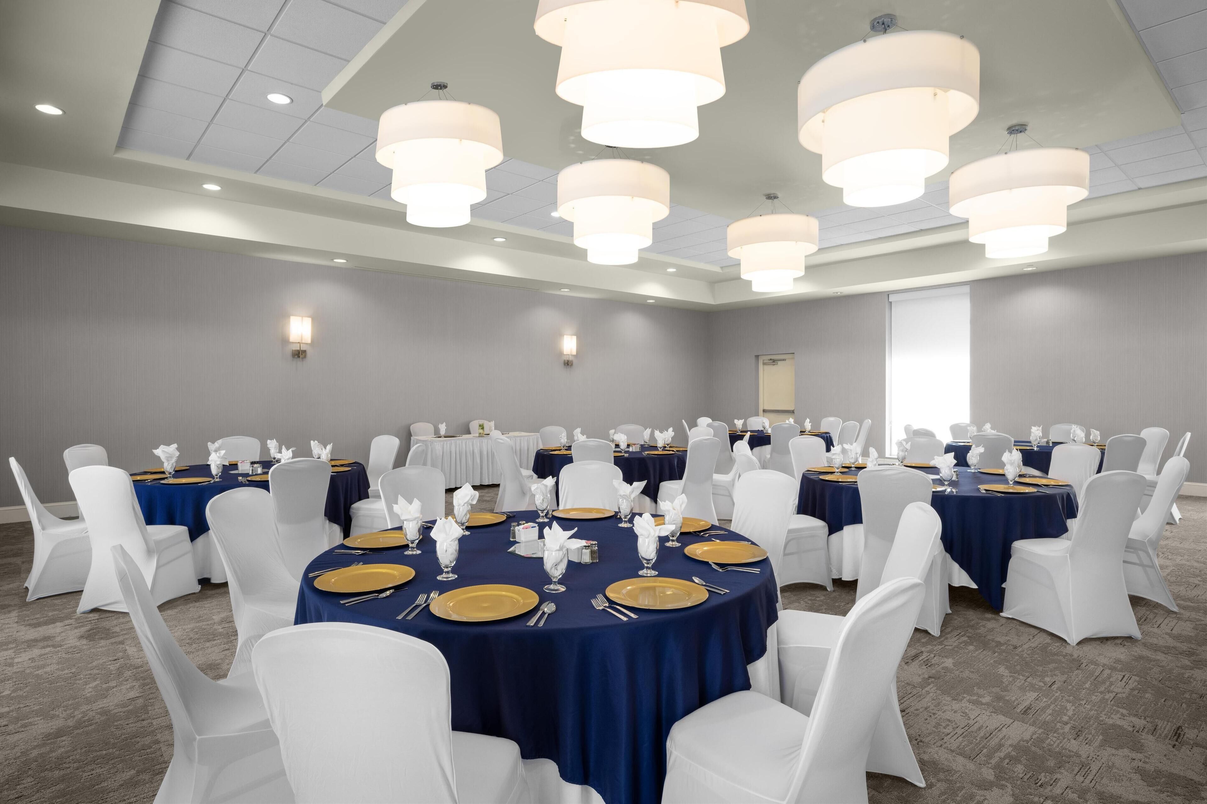 Un salón de banquetes con mesas redondas, sillas blancas y manteles azules.