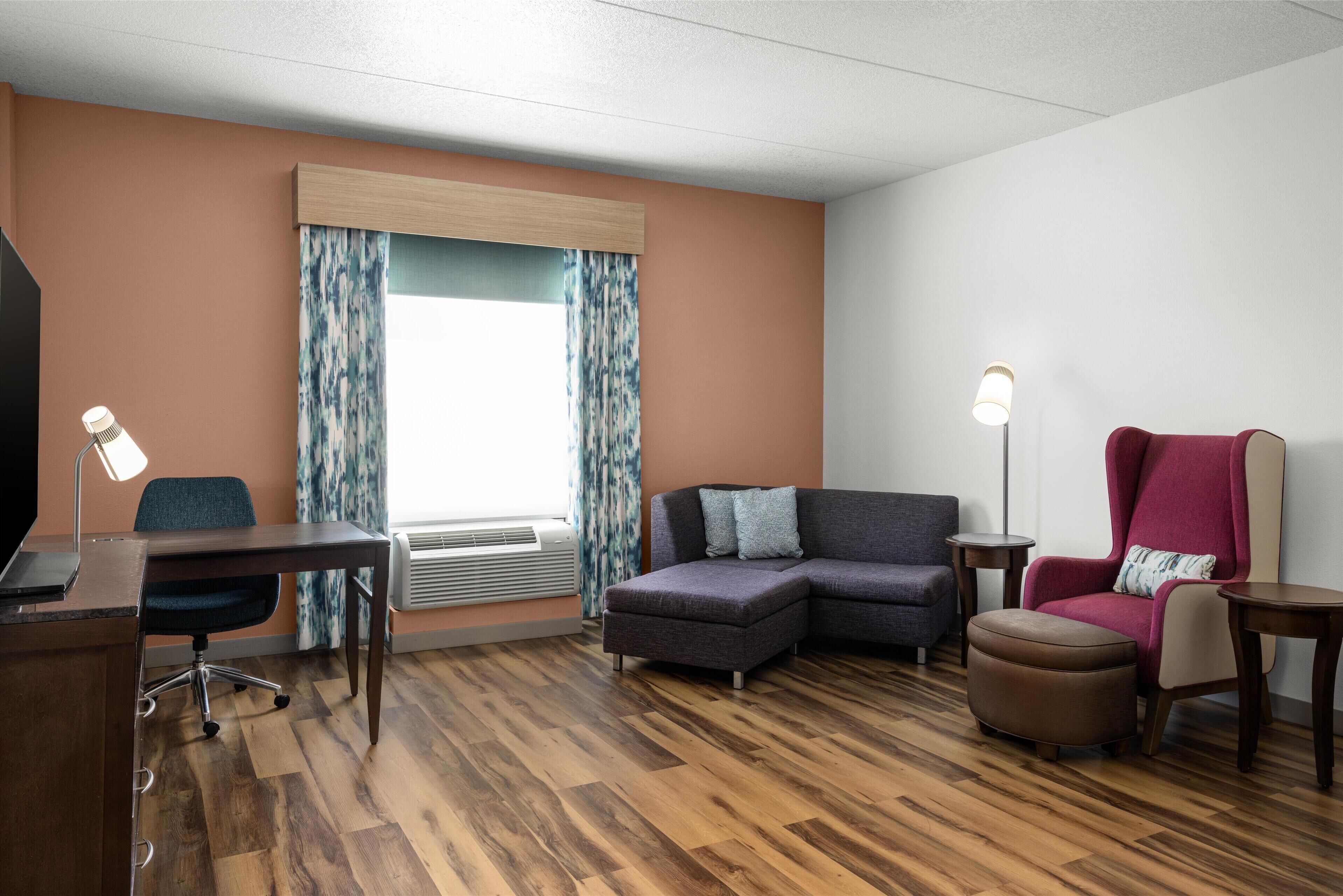 A modern living room with a sectional sofa, a desk with a chair, a red armchair, and a floor lamp.