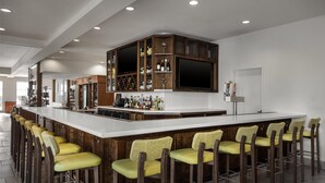 A modern bar area with a long counter, multiple stools, and a television. - Hilton Garden Inn Pascagoula (Pascagoula)
