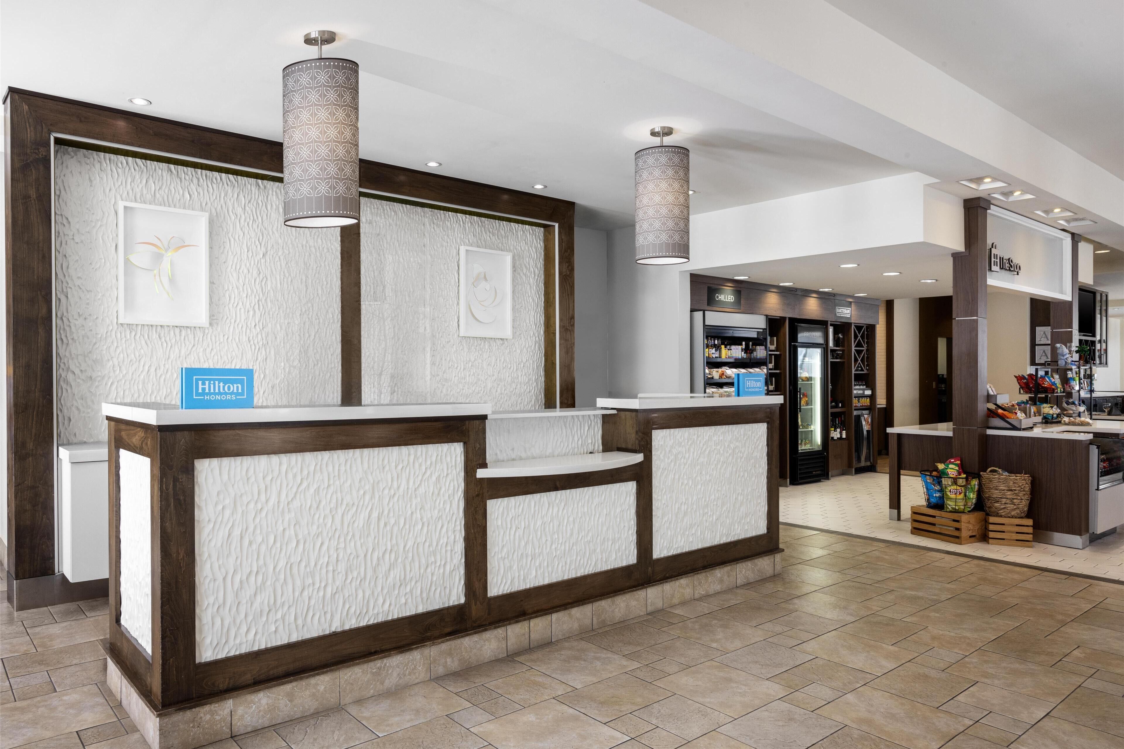 Eine Hotelrezeption mit modernem Design, inklusive einer strukturierten Wand, einem Empfangstresen und einem 'Hilton'-Schild.