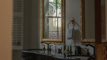 A bathroom with a dark wooden vanity, two large mirrors with gold frames, and a window with shutters.