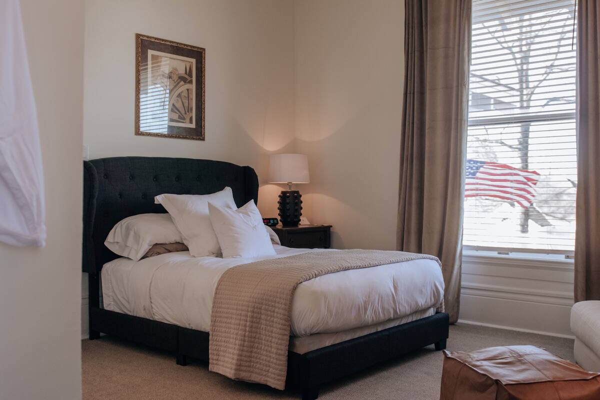 A neatly made bed with a dark headboard, a bedside lamp, and a framed picture on the wall.