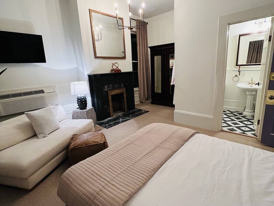A hotel room with a large bed, a sofa, a fireplace, a TV mounted on the wall, and a bathroom visible through an open door.