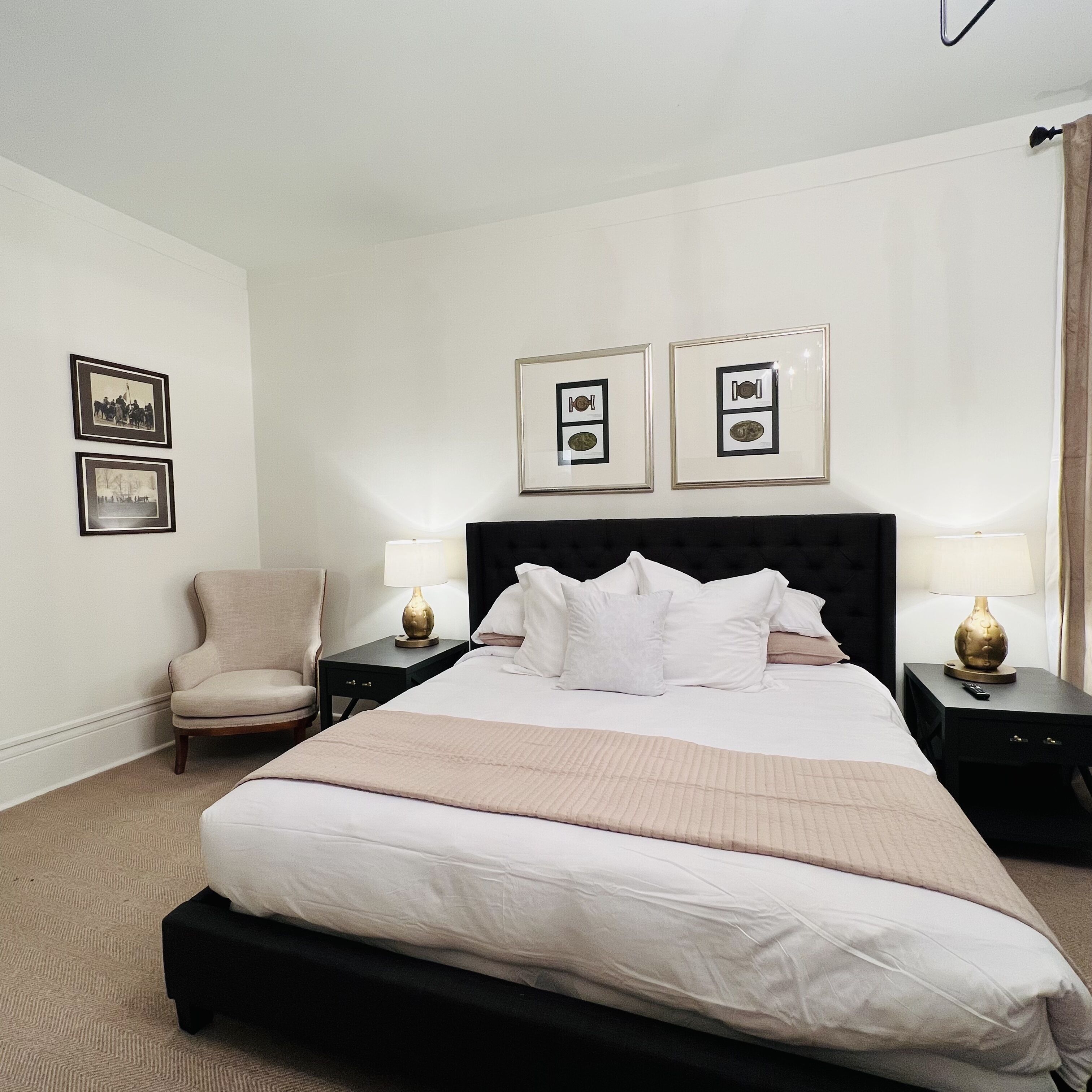 Une chambre d’hôtel avec un lit, deux tables de chevet, une chaise et des tableaux encadrés au mur.