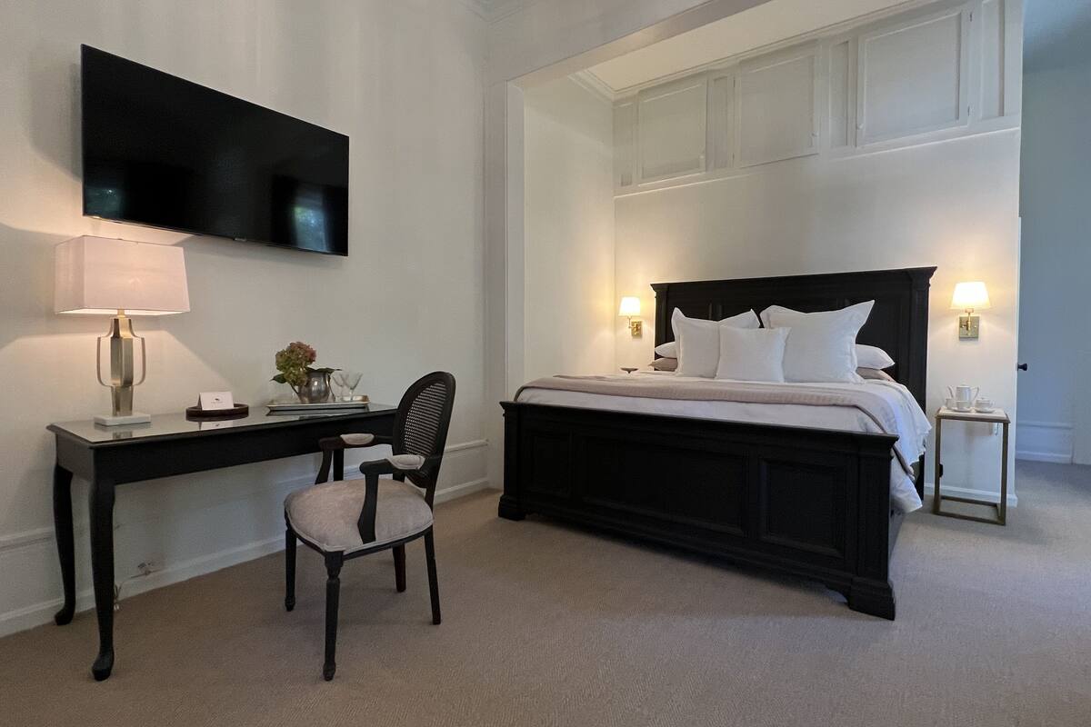 A hotel room with a bed, a desk, a chair, a TV, and two bedside lamps.