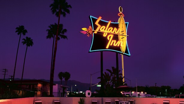 Un espace piscine avec des chaises longues et un panneau lumineux au néon indiquant « Safari Inn ».