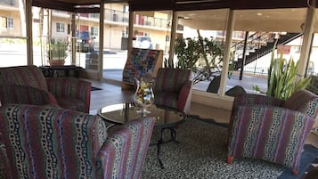 A seating area with patterned sofas and a glass table, a decorative vase, and a view of the street and buildings outside.