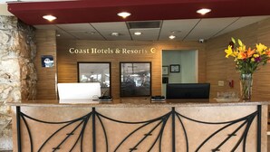 Un comptoir d’accueil dans un hôtel Coast Hotels & Resorts, avec un mur en pierre en arrière-plan, un comptoir de réception et un motif décoratif en métal.