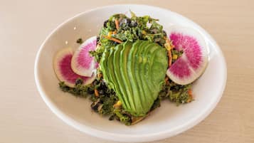 A white plate with a salad, avocado slices, and radish slices on a wooden table.