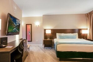 A hotel room with a bed, desk, chair, and a television mounted on the wall.
