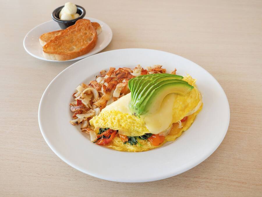 A plate with an omelette, avocado, and vegetables.