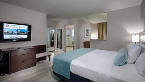 Une chambre d’hôtel avec un lit, un bureau, une télévision et une salle de bain visible à travers une porte ouverte.
